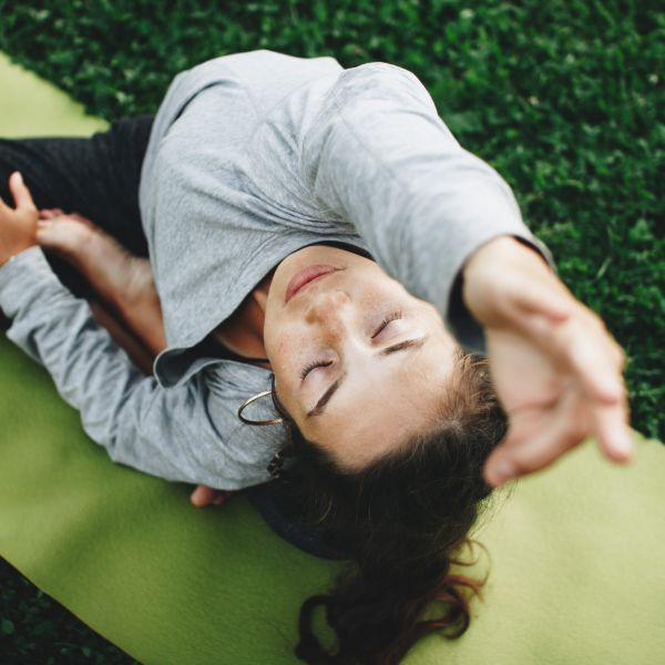 Woman is practicing yoga on a green lawn. Young woman relaxes in yoga pose outdoors